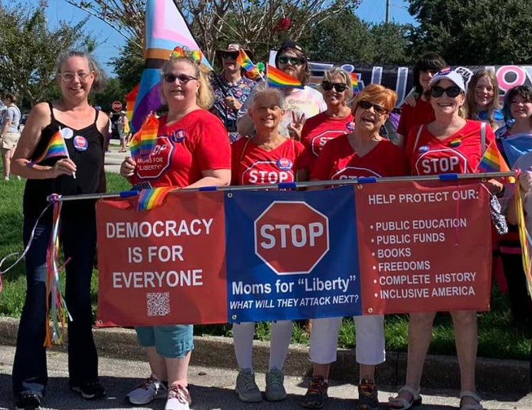 group of people at pride parade holding a STOP Moms for Liberty Banner and wearing STOP Moms for "Liberty" shirts
